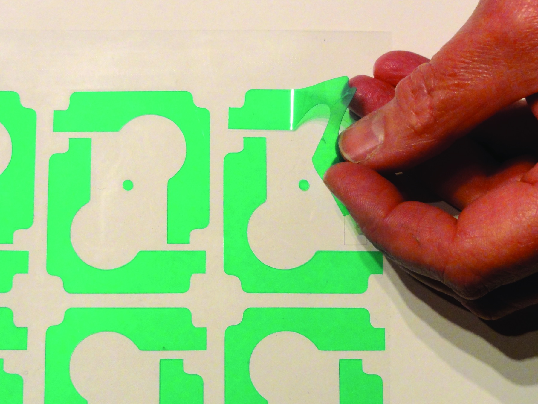 Hand peeling a green pre-cut masking shape from a backing sheet